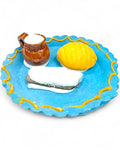 Miniature ceramic plate with a teacup, lemon, and bread on a white background